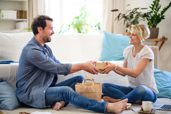 Happy couple sitting on floor indoors at home, food delivery service concept.