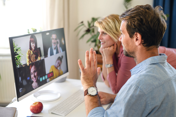 Happy couple having video call with family on laptop indoors at home, waving.