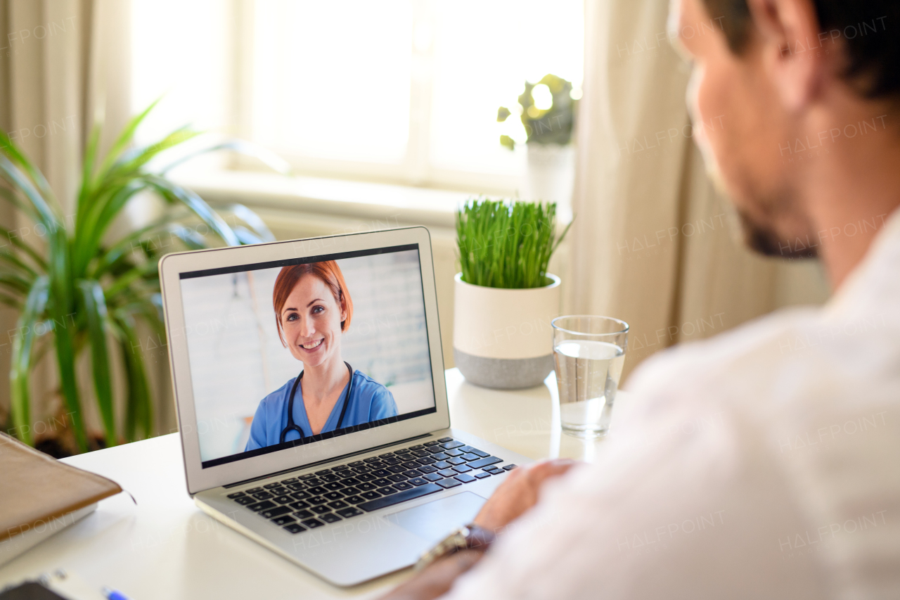 Mature man having video call with doctor on laptop at home, online consultation concept.