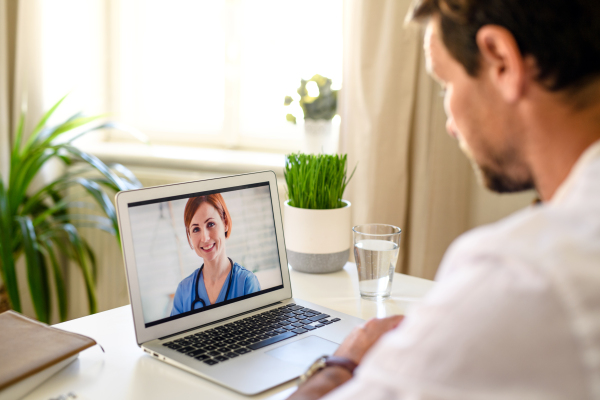 Mature man having video call with doctor on laptop at home, online consultation concept.