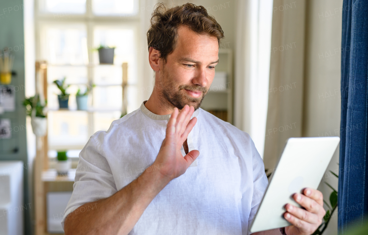 Portrait of mature man having video call on tablet at home, waving.