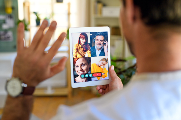 Rear view of unrecognizable man having video call on tablet at home, waving.