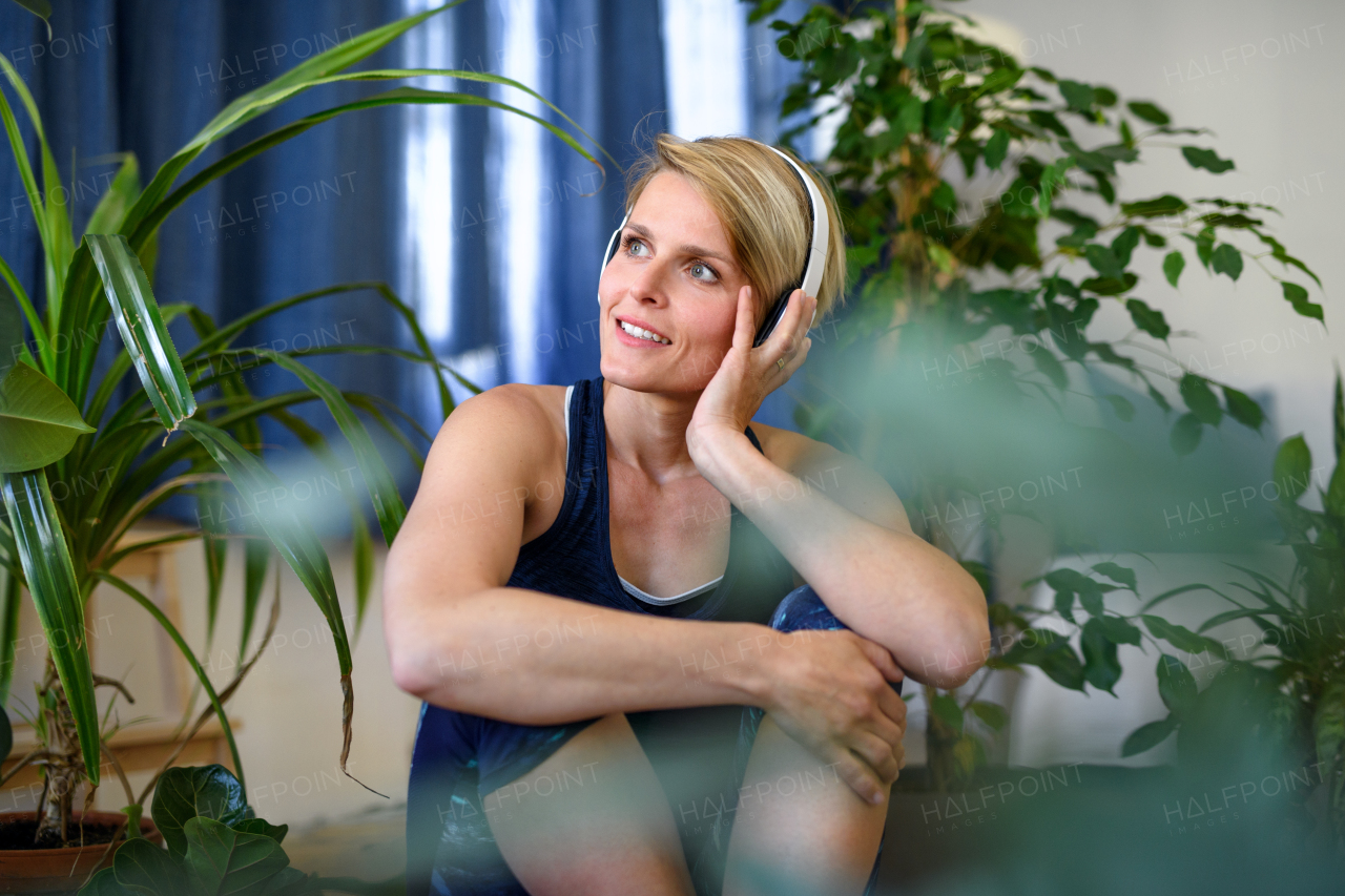 Front view of happy young woman with headphones indoors at home, resting.