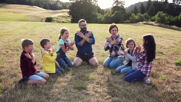 Group of school children with teacher on field trip in nature, sitting in circle, playing. Slow motion.