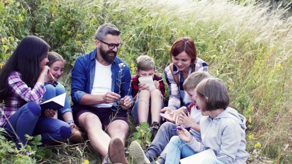 A group of small school children with teacher on field trip in nature, learning.