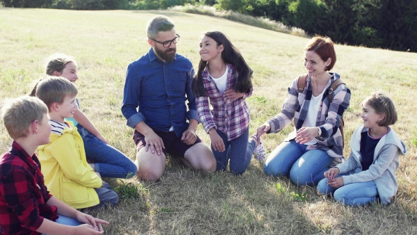 Group of school children with teacher on field trip in nature, sitting in circle and playing.