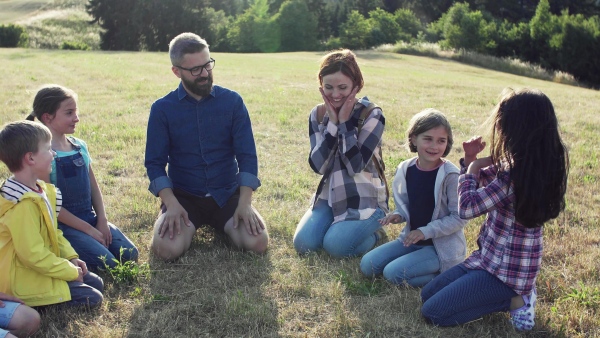 Group of school children with teacher on field trip in nature, sitting in circle and playing.