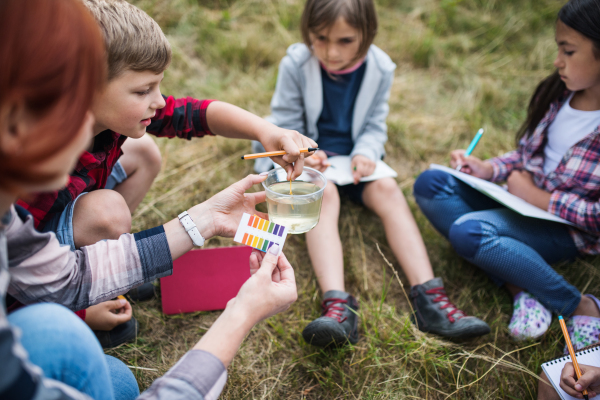 A group of small school children with teacher on field trip in nature, learning science.