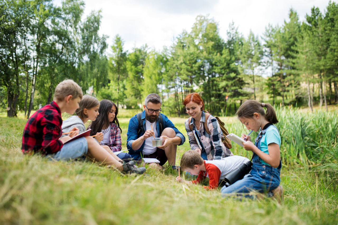 A group of small school children with teacher on field trip in nature, learning science.