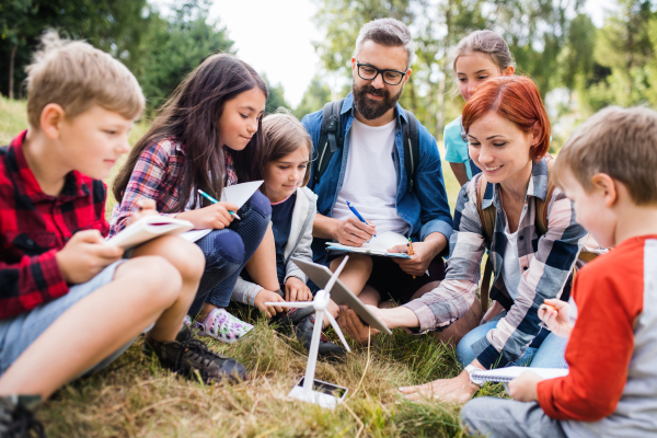 A group of school children with teacher and windmill model on field trip in nature.