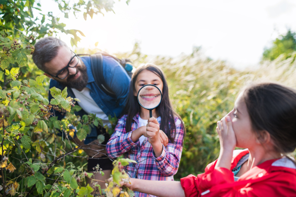 Small school children with teacher and magnifying glass on field trip in nature, learning science.