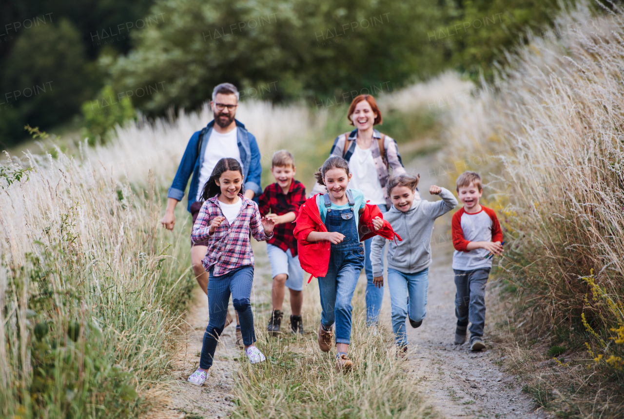 A group of small school children with teacher on field trip in nature, running.