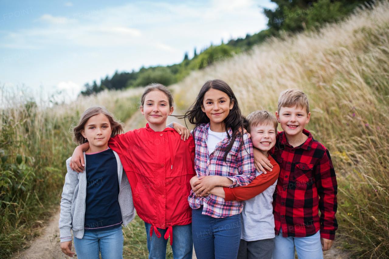 Portrait of group of school children standing on field trip in nature, looking at camera.