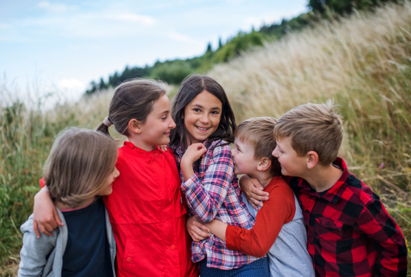 Portrait of group of school children standing on field trip in nature, playing.