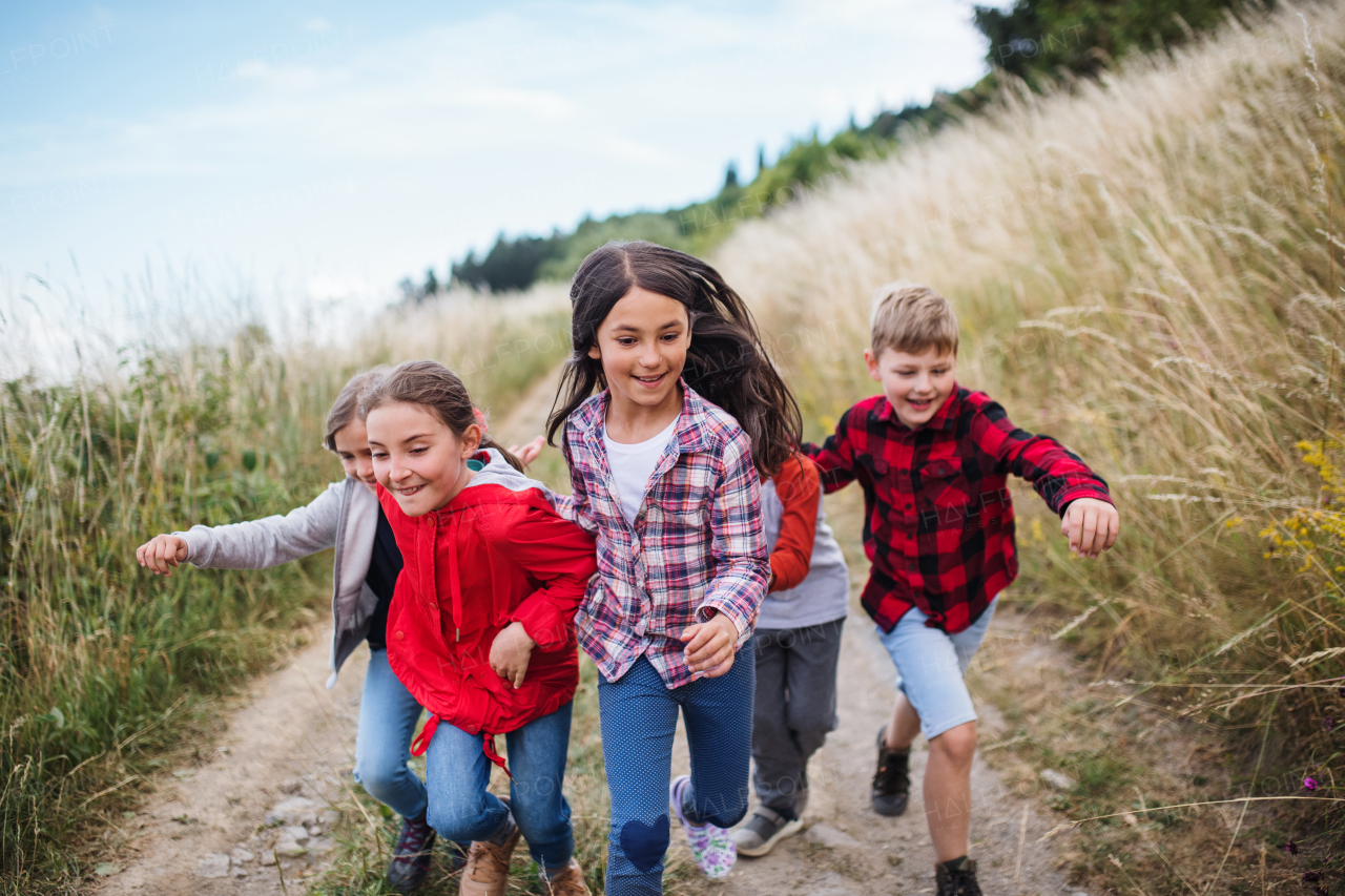 Portrait of group of school children running on field trip in nature.