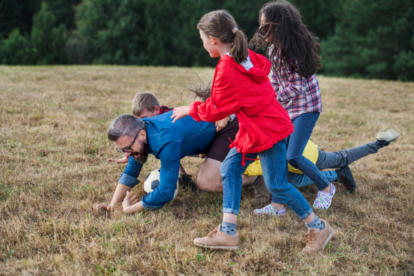 A group of small school children with teacher on field trip in nature, playing with a ball.