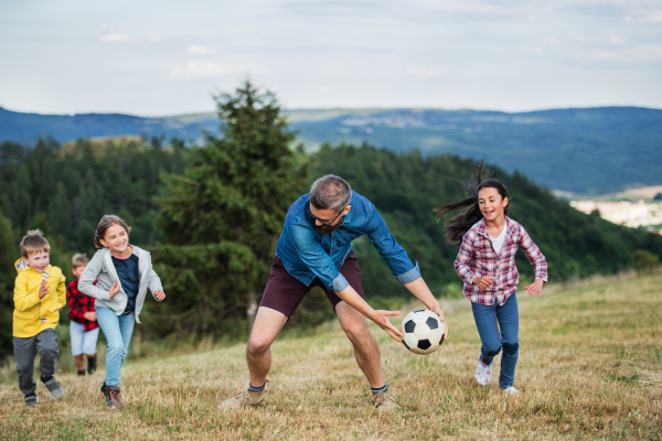 A group of small school children with teacher on field trip in nature, playing with a ball.