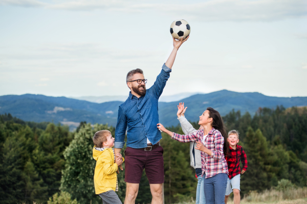 A group of small school children with teacher on field trip in nature, playing with a ball.