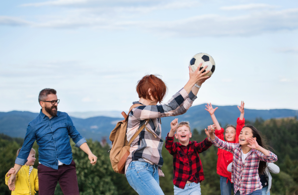 A group of small school children with teacher on field trip in nature, playing with a ball.