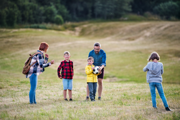 A group of small school children with teacher on field trip in nature, playing with a ball.