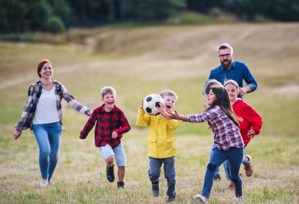 A group of small school children with teacher on field trip in nature, playing with a ball.