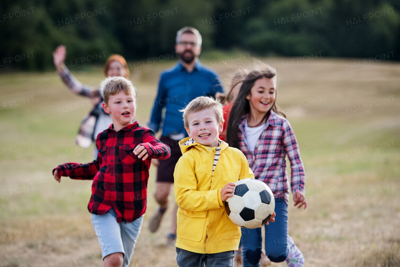 A group of small school children with teacher on field trip in nature, playing with a ball.