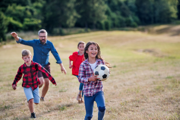 A group of small school children with teacher on field trip in nature, playing with a ball.