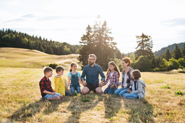 Group of school children with teacher on field trip in nature, sitting and holding hands.