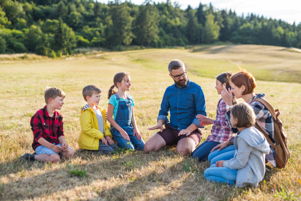 Group of school children with teacher on field trip in nature, sitting and talking.