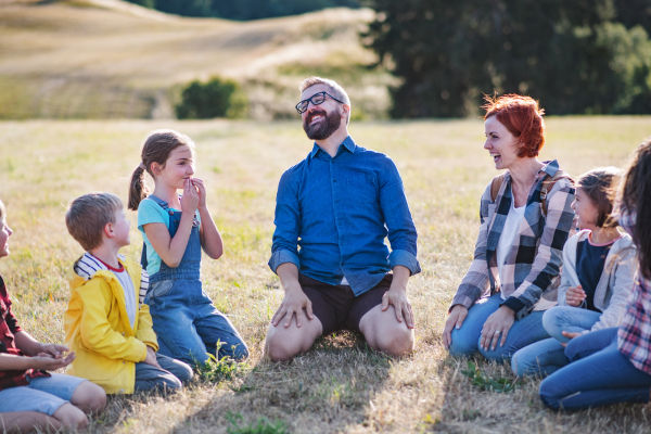 A group of small school children with teacher on field trip in nature, laughing.