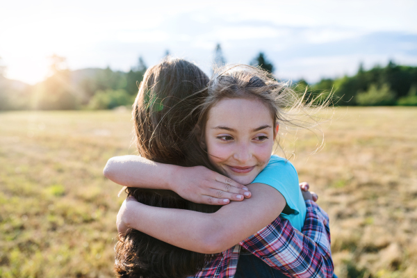 Two cheerful school children walking on field trip in nature, hugging.