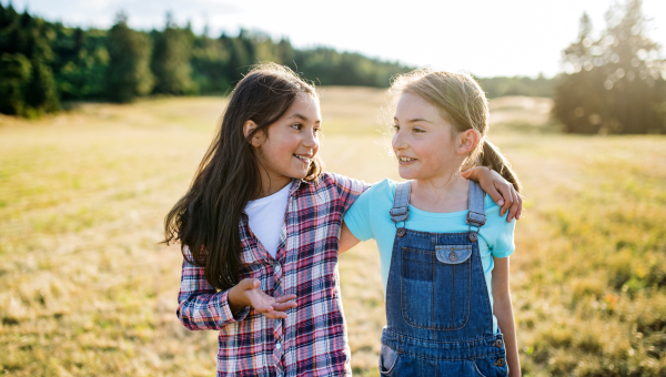 Two cheerful school children walking on field trip in nature, talking.