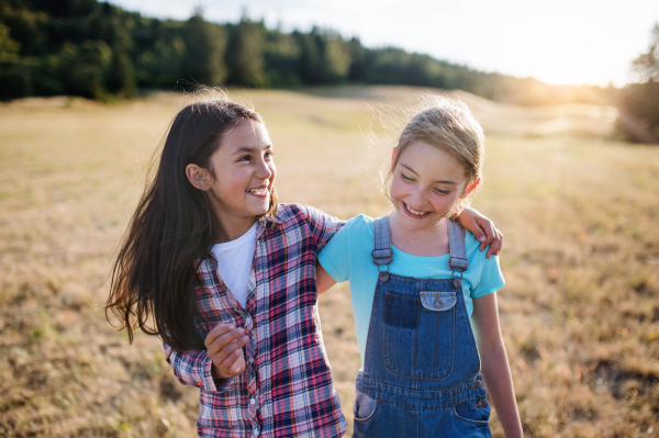 Two cheerful school children walking on field trip in nature, laughing.