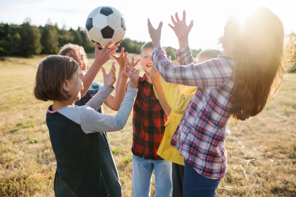 Portrait of group of school children standing on field trip in nature, playing with a ball.