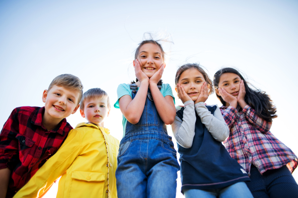 Portrait of group of school children standing on field trip in nature, looking at camera.