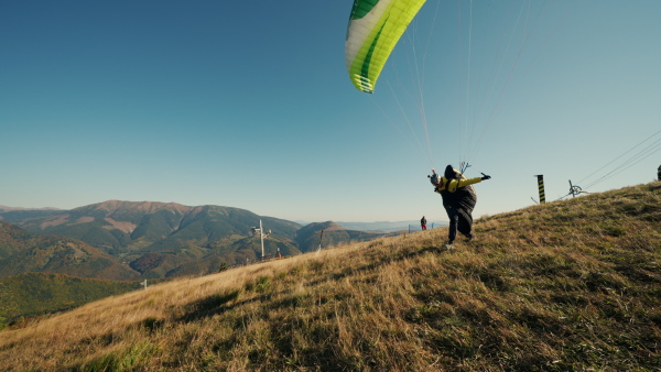 A paraglider taking off in the blue sky with mountain in background.