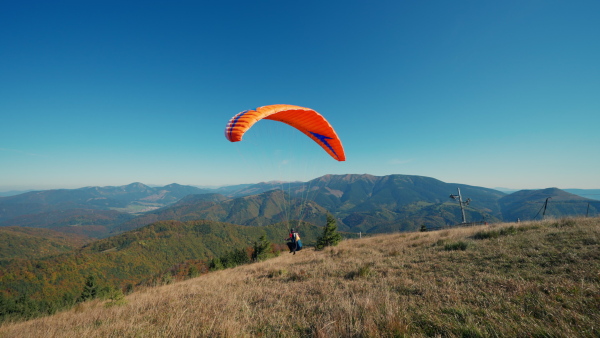 A paraglider taking off in the blue sky with mountain in background.