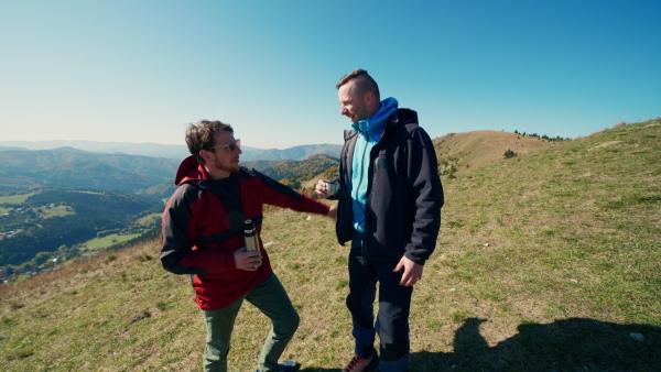 Two paragliders men standing on the top of mountain and drinking a tea.