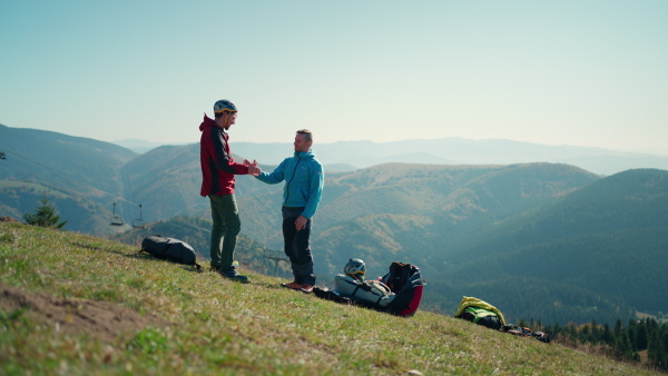 Paragliders high fiving after walking up hill to a paragliding starting point, on a sunny morning in mountains.