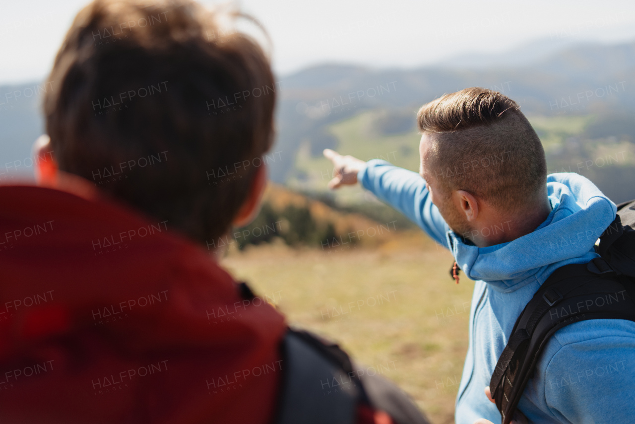 Two paragliders men standing on a top of mountain, looking at view and pointing.