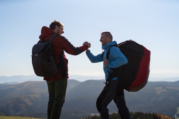 Paragliders high fiving after walking up hill to a paragliding starting point, on a sunny morning in mountains.