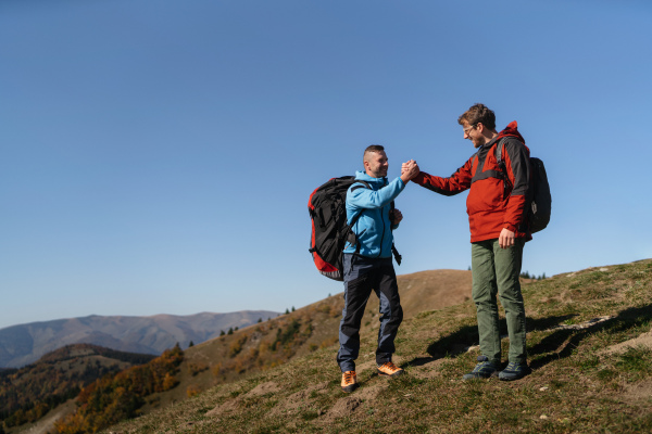 Paragliders high fiving after walking up hill to a paragliding starting point, on a sunny morning in mountains.