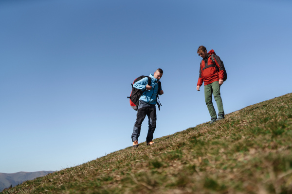 Paragliders walking up hill to paragliding starting point, on a sunny morning in mountains.