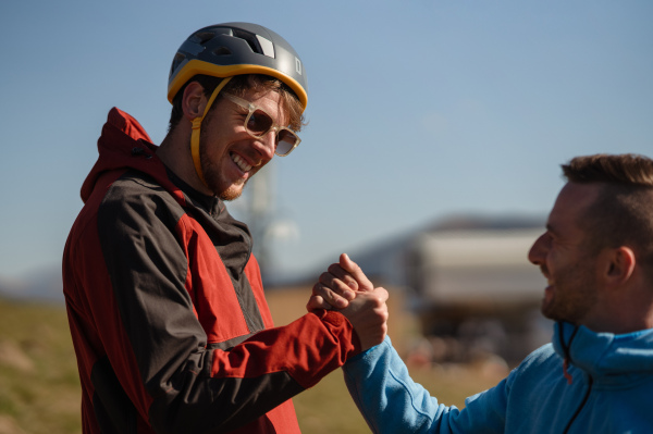 Paragliders high fiving after walking up hill to a paragliding starting point, on a sunny morning in mountains.