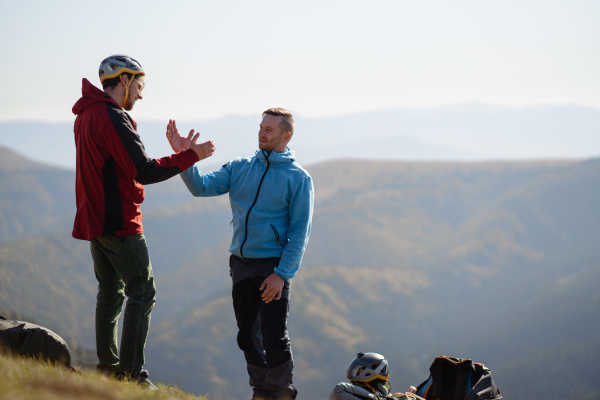 Paragliders high fiving after walking up hill to a paragliding starting point, on a sunny morning in mountains.