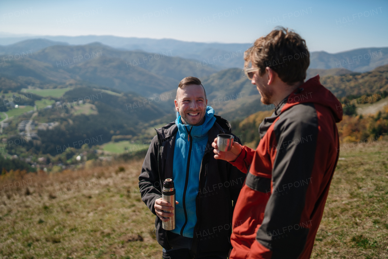 Two paragliders men standing on the top of mountain and drinking a tea.