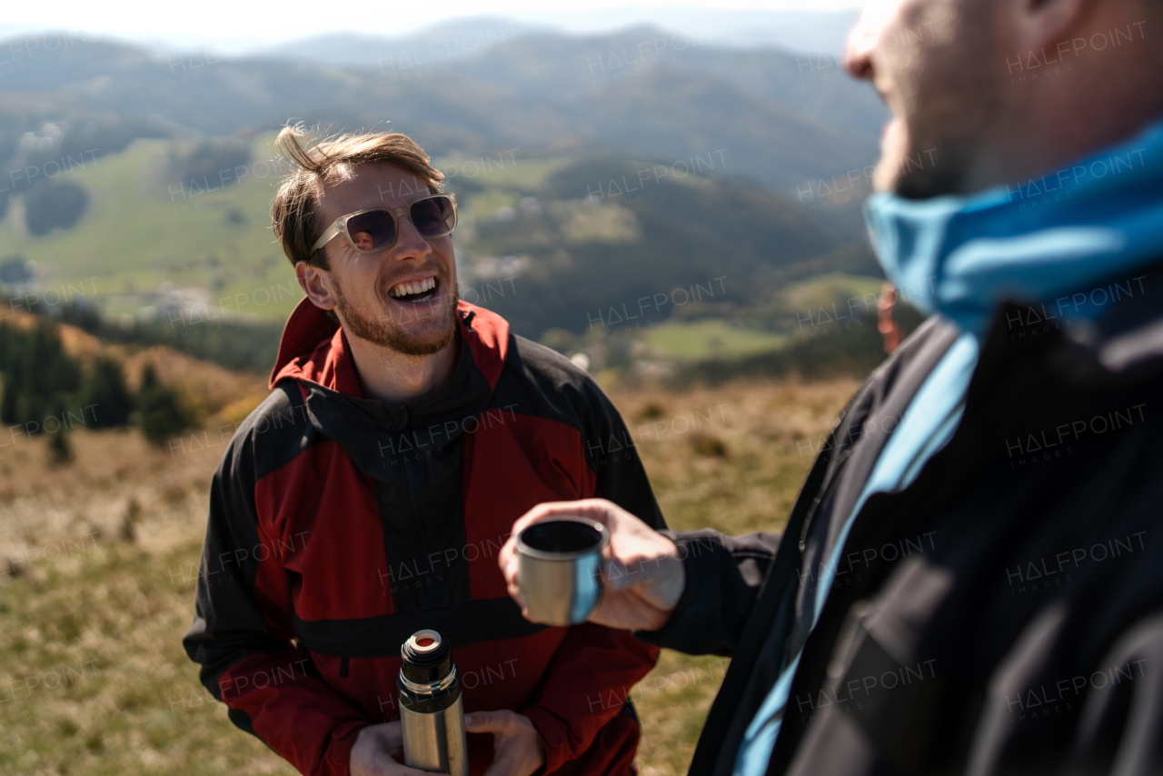 Two paragliders men standing on the top of mountain and drinking a tea.