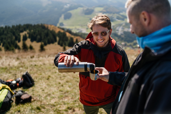 Two paragliders men standing on the top of mountain and drinking a tea.