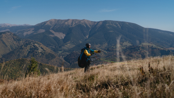 A paragliding pilot is preparing for flight in mountains.