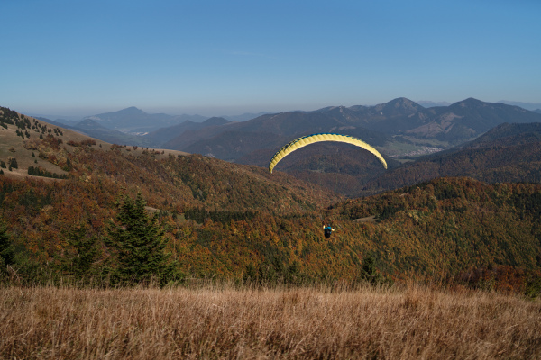 A paraglider flying in the blue sky with mountain in background.